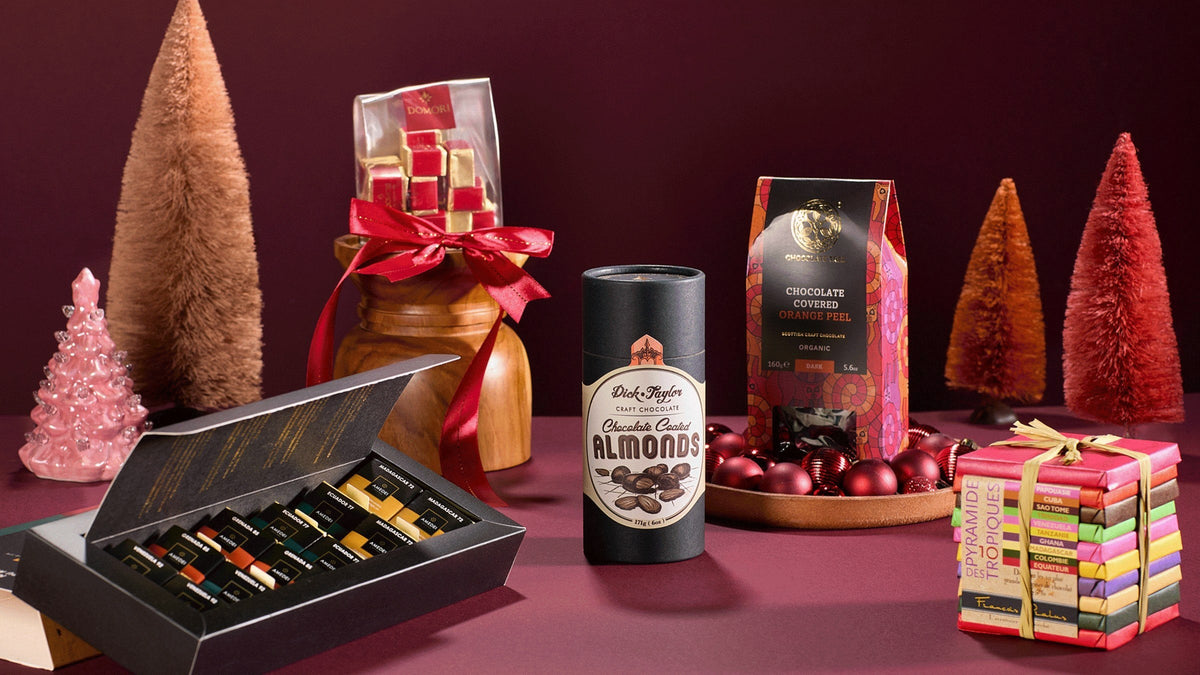 Chocolate gift boxes, Dick Taylor almonds and a stack of Pralus bars among small holiday trees on a burgundy backdrop