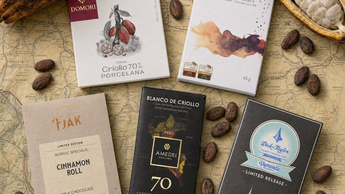 Craft chocolate bars from Domori, Soma, Fjåk, Amedei and Dick Taylor laid on a vintage map with cacao beans and pods