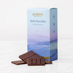 A blue watercolor mountain box of French Broad dark chocolate 6 Bar Collection behind unwrapped chocolate pieces.