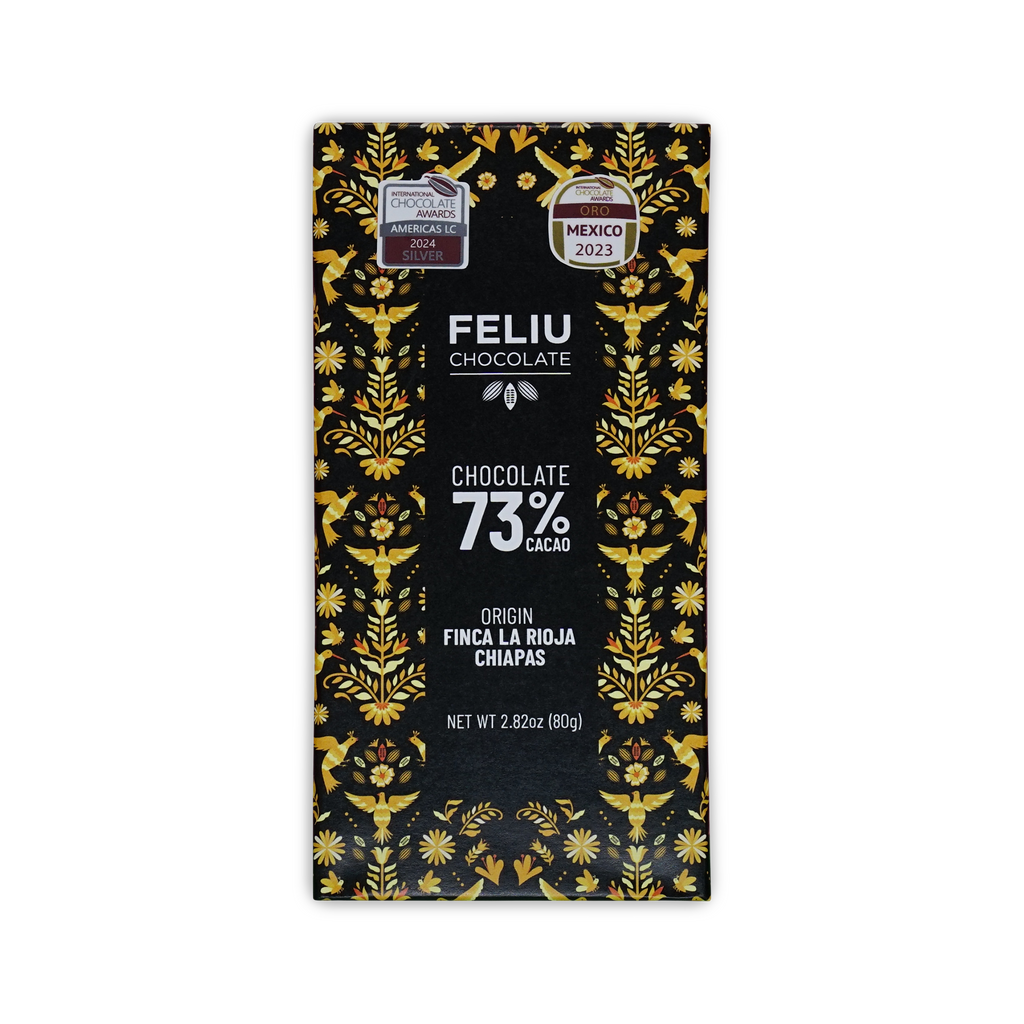 A black Feliu Chocolate 73% cacao bar box with yellow bird and floral patterns and Finca La Rioja Chiapas text.