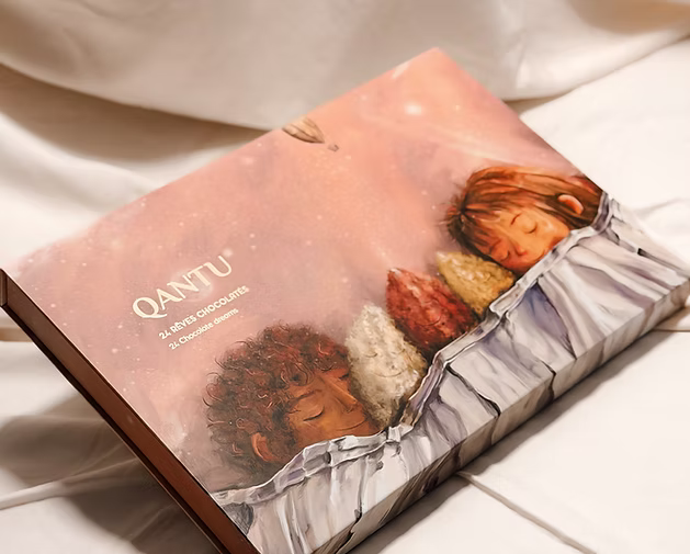 Pink Qantu advent calendar box illustrated with sleeping figures and cacao pods, resting on white fabric.