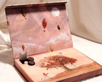 Open pink Qantu advent calendar box with numbered doors and two round chocolates in an open compartment.