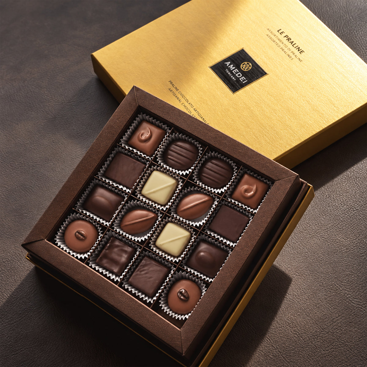 Open Amedei gift box of 16 assorted chocolate pralines with a gold lid.