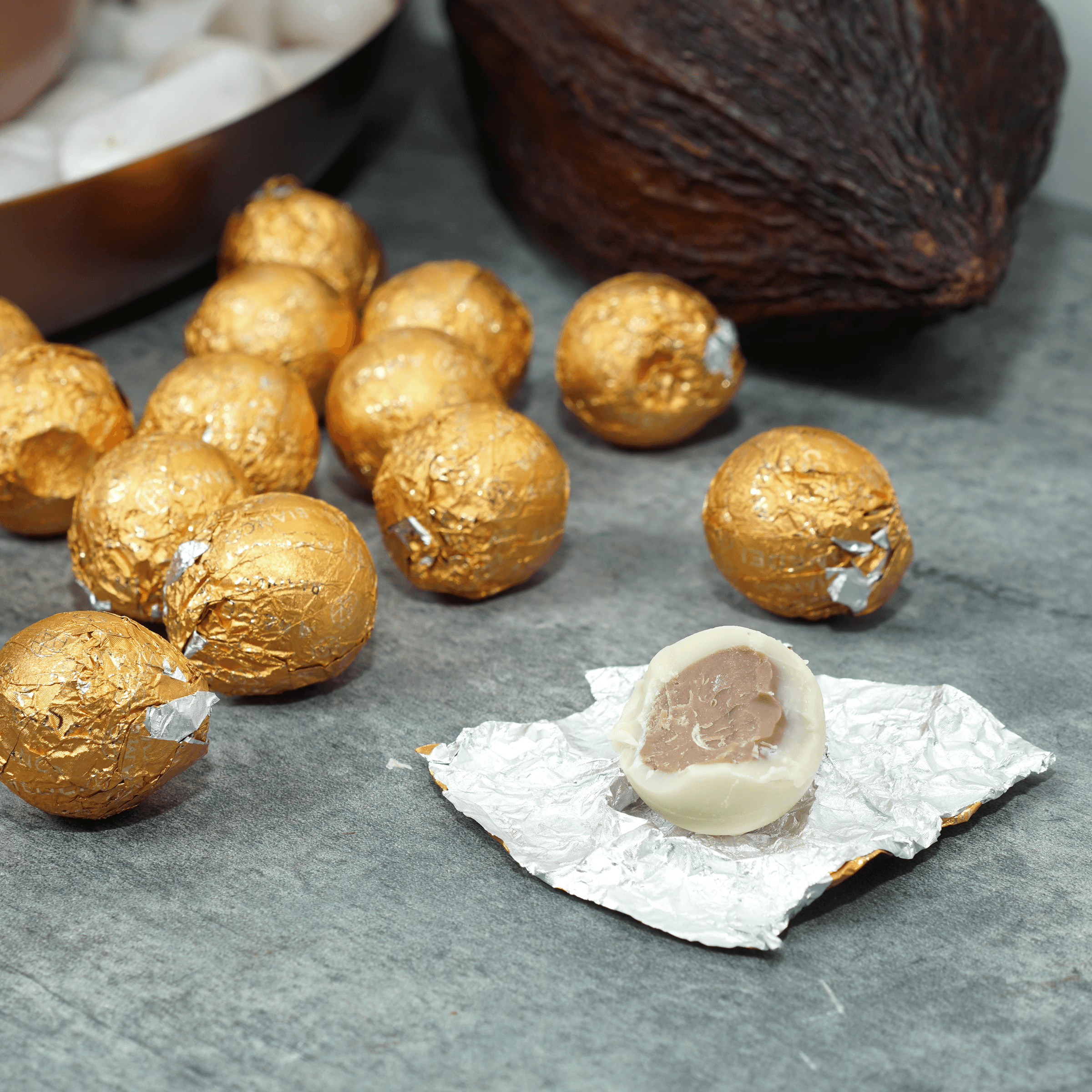 Amedei Pralines White w/ Hazelnut Filling: golden foil-wrapped truffles, one unwrapped showing white shell and dark center