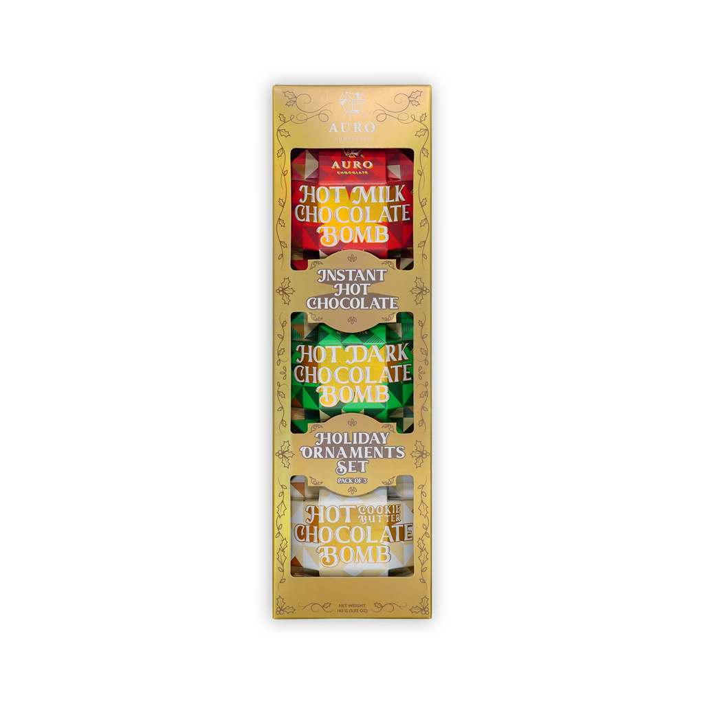 A gold Auro box reading Holiday Ornaments Set, revealing three hot chocolate bombs wrapped in red, green, and white foil.