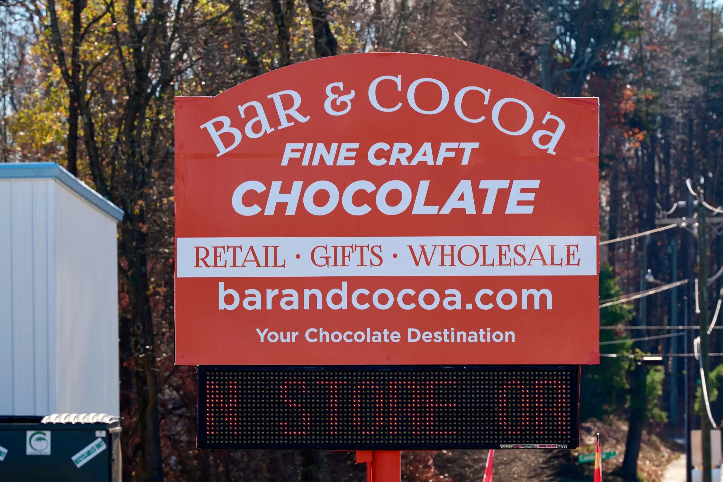 Red rectangular sign for bar & cocoa, featuring white lettering and a digital display below showing ’a store is’ in red.