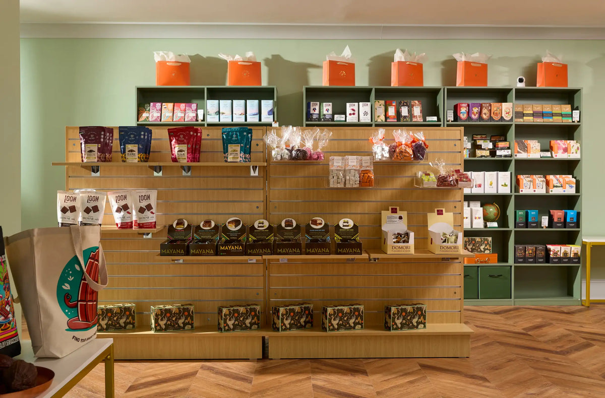 Wooden shelving unit with multiple tiers displaying various packaged chocolate products and gift boxes.
