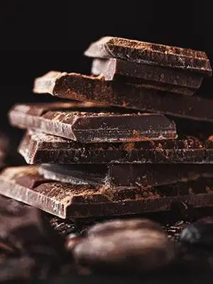 Dark chocolate bars stacked in a pile, with some pieces broken and dusted with cocoa powder.