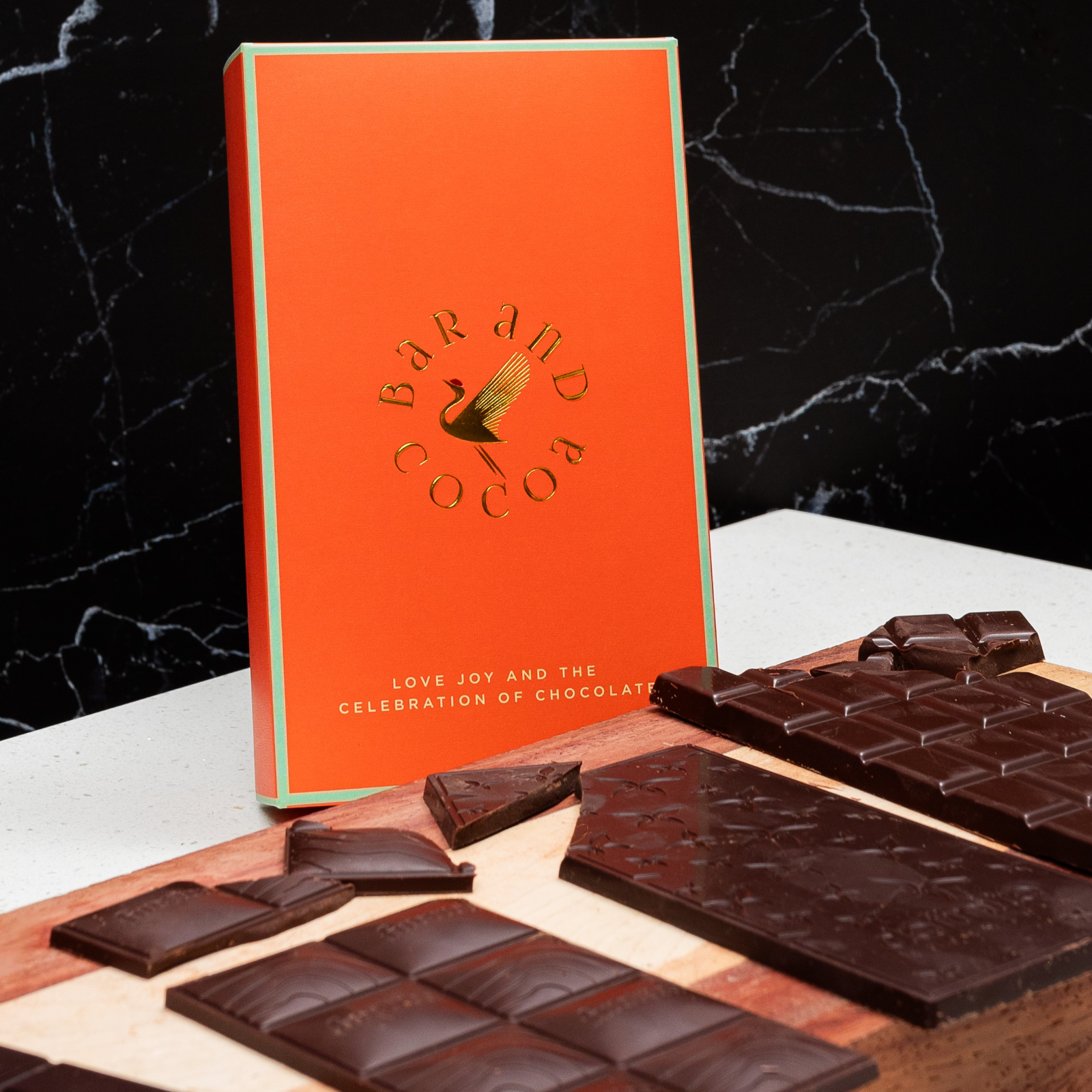 Vibrant orange Discover Chocolate Club bar box with gold logo and dark pieces