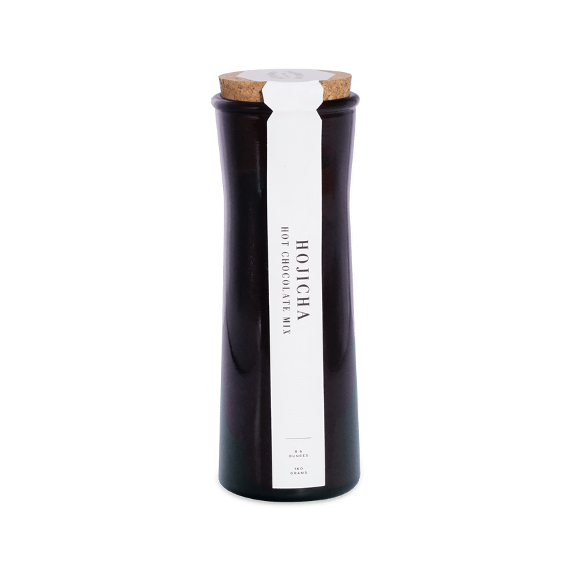 Tall dark amber glass jar with a cork lid and a white front label reading Hojicha Hot Chocolate Mix, 5.6 ounces, 160 grams.