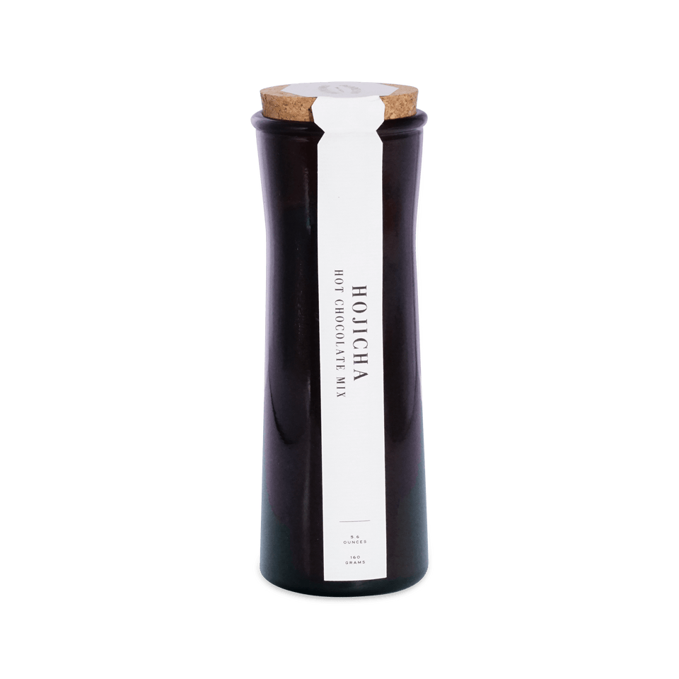Tall dark amber glass jar with a cork lid and a white front label reading Hojicha Hot Chocolate Mix, 5.6 ounces, 160 grams.