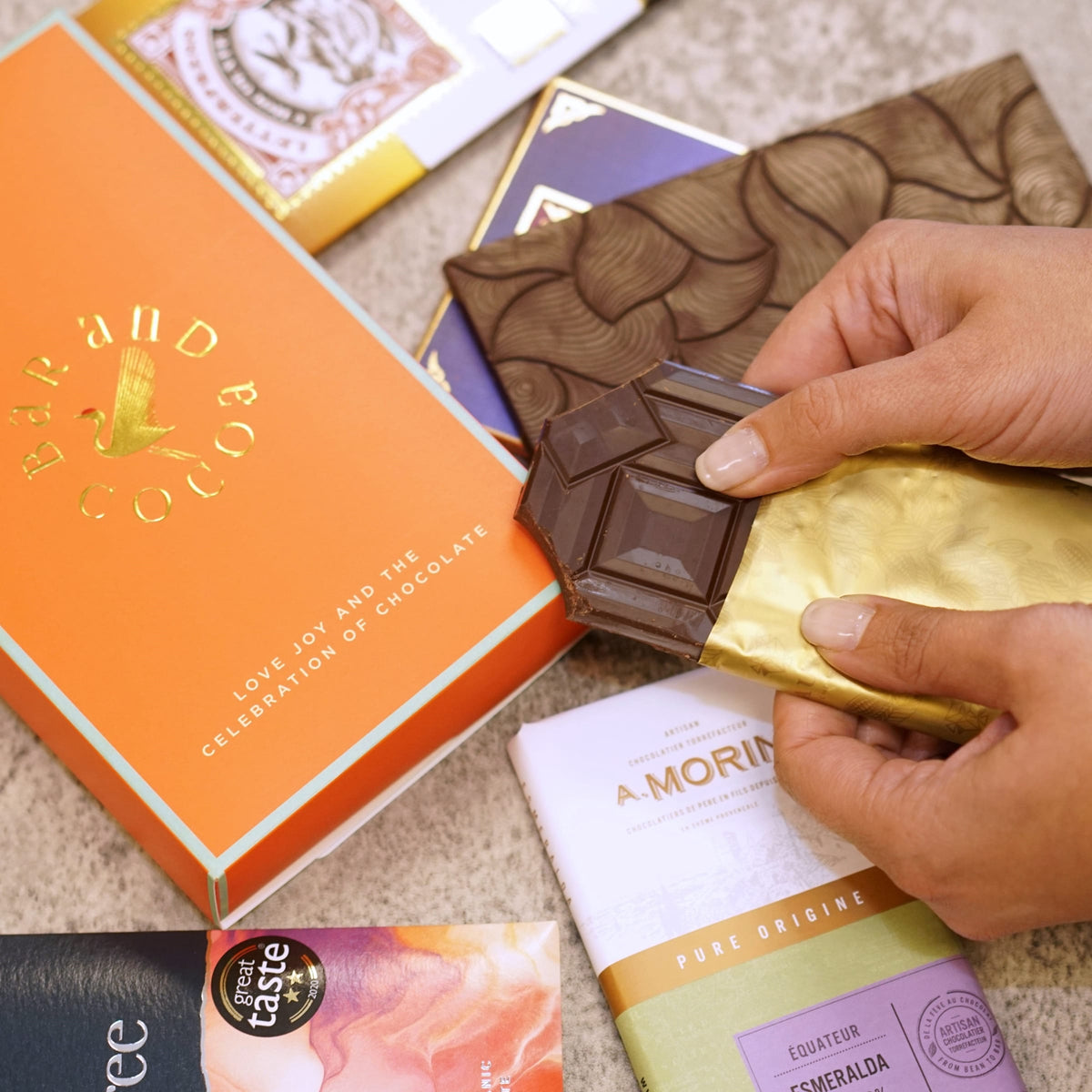 Hand holding a gold-wrapped Discover Chocolate Club bar over a dark chocolate surface