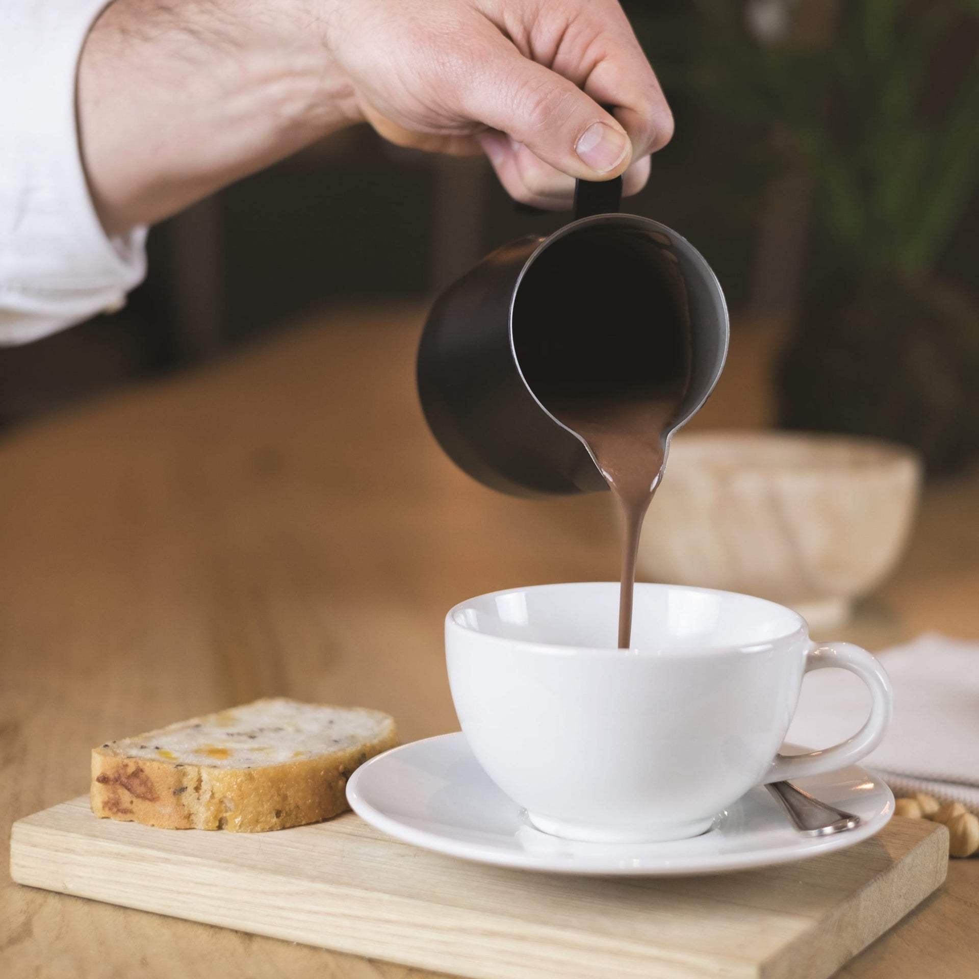 Sleek black ceramic milk pitcher pouring cream into white cup for Domori Hot Chocolate Mix