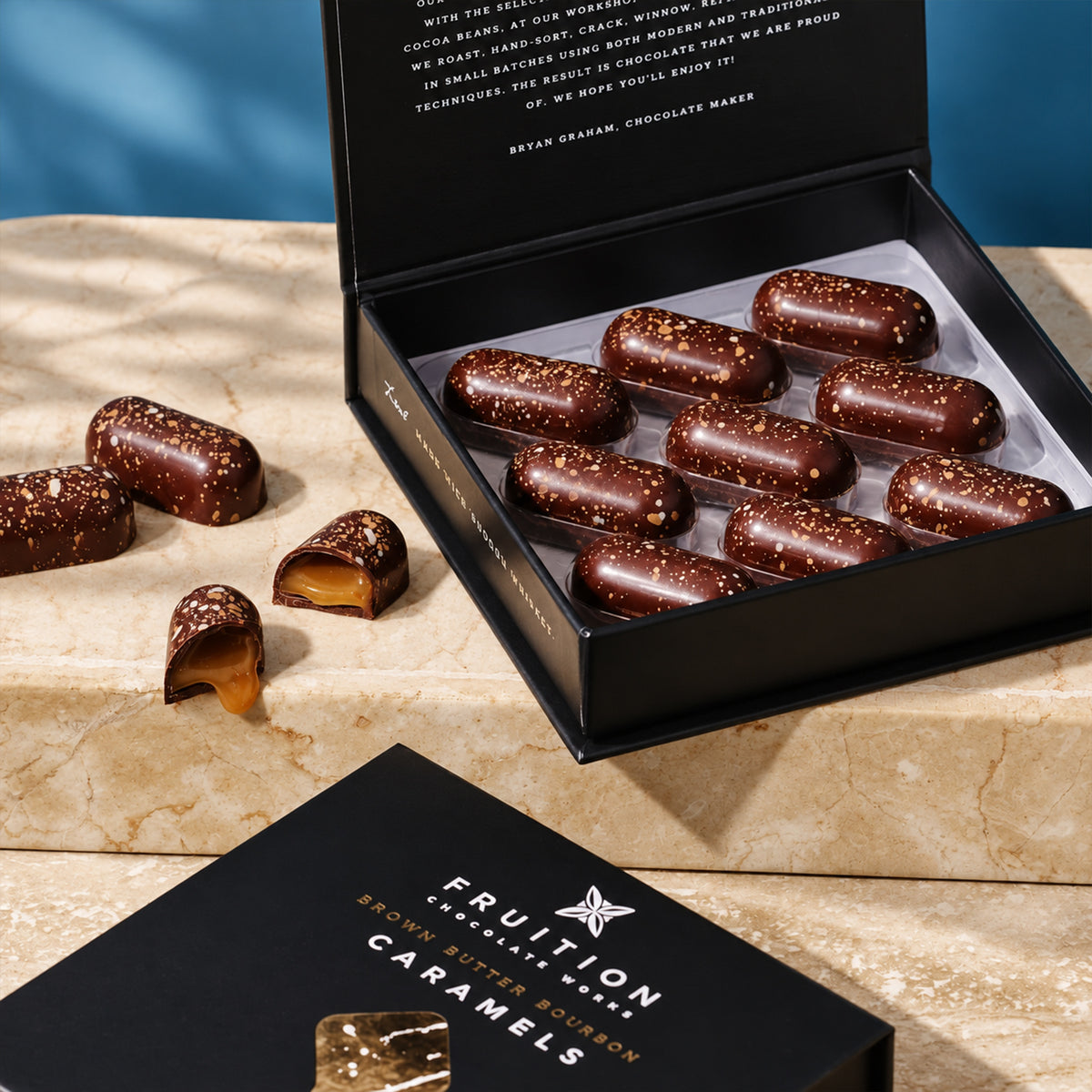 Open black Fruition box of brown butter bourbon caramels, with one caramel cut in half.