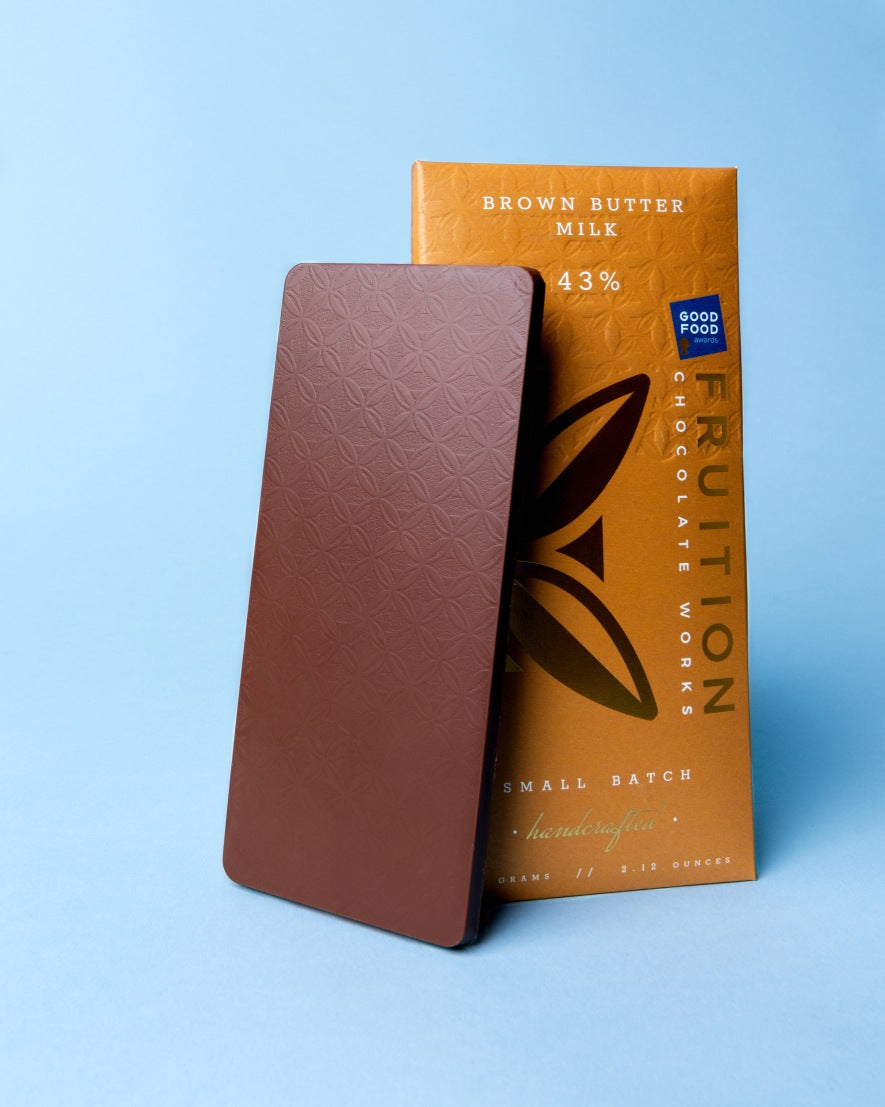 Fruition Brown Butter Milk 43% chocolate bar beside its gold wrapper on a blue background
