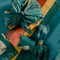 Two chocolate bundles wrapped in Bar & Cocoa crane forest print furoshiki on orange, yellow, and green ribbon stripes