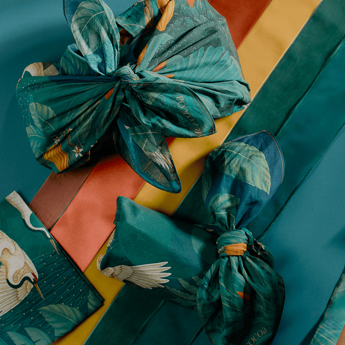 Two chocolate bundles wrapped in Bar & Cocoa crane forest print furoshiki on orange, yellow, and green ribbon stripes