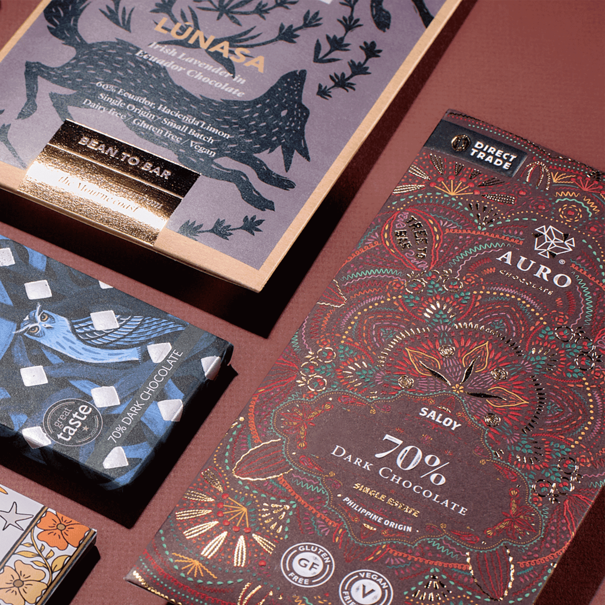 NearyNogs, Auro and Theo & Philo craft chocolate bars with illustrated wrappers on a burgundy surface
