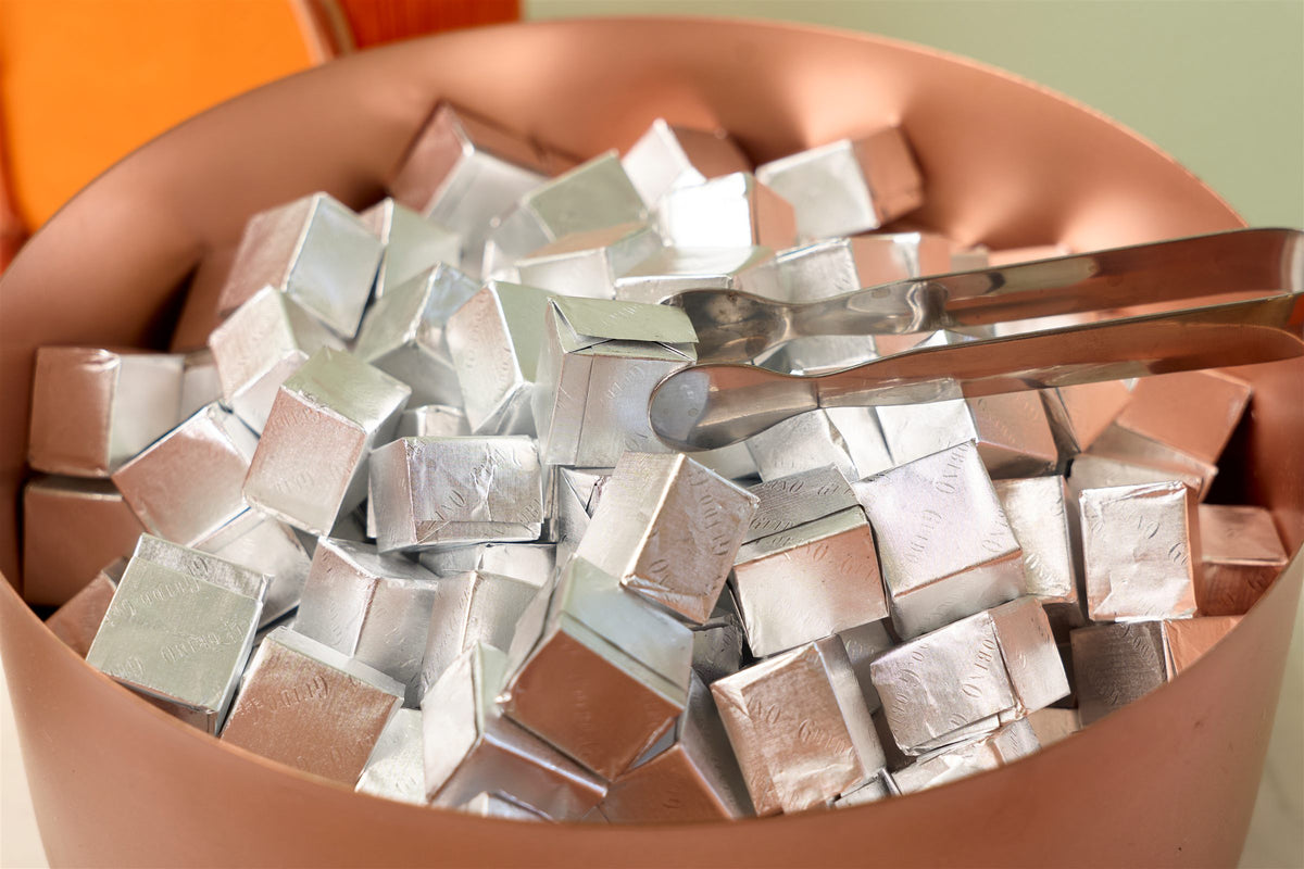 Copper bowl filled with foil-wrapped chocolates and serving tongs