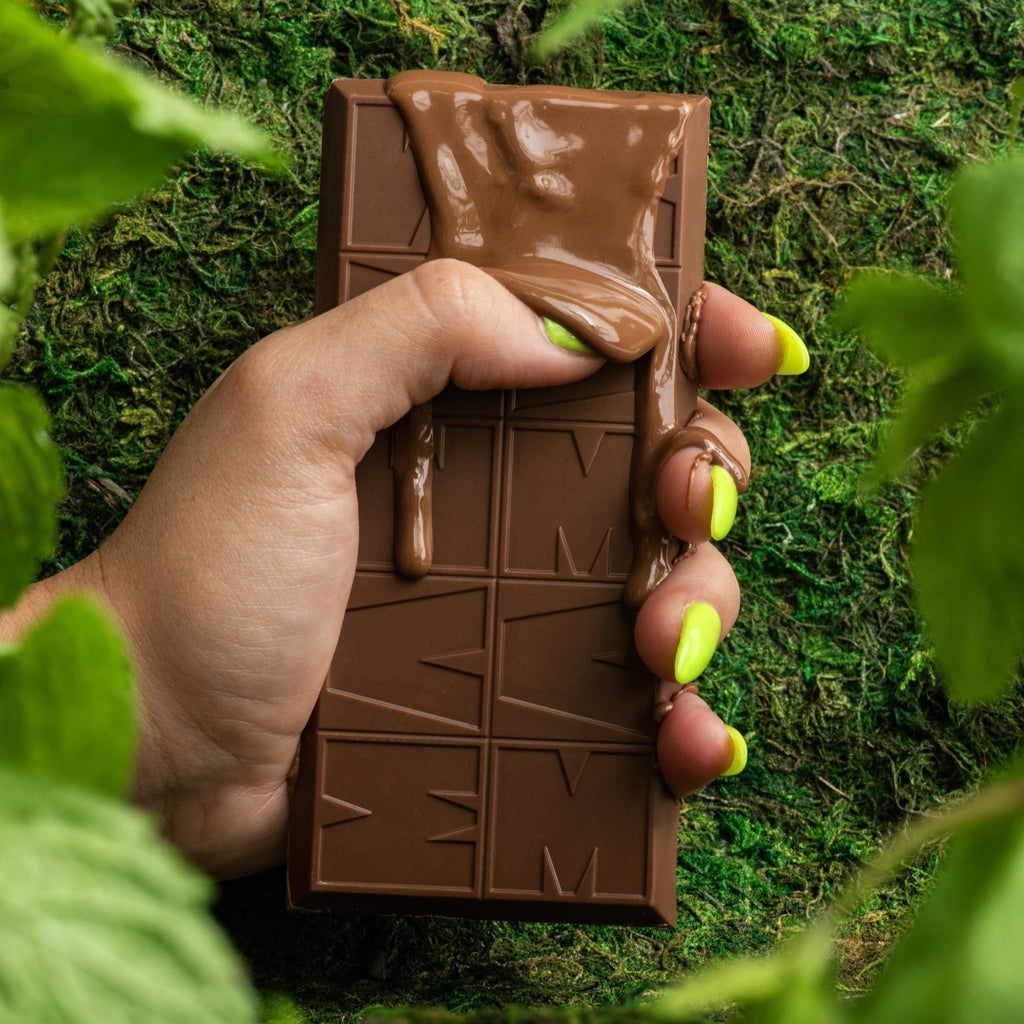Hand holding a chocolate bar with melted chocolate dripping down over a green moss background