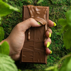 Hand holding a chocolate bar with melted chocolate dripping down over a green moss background