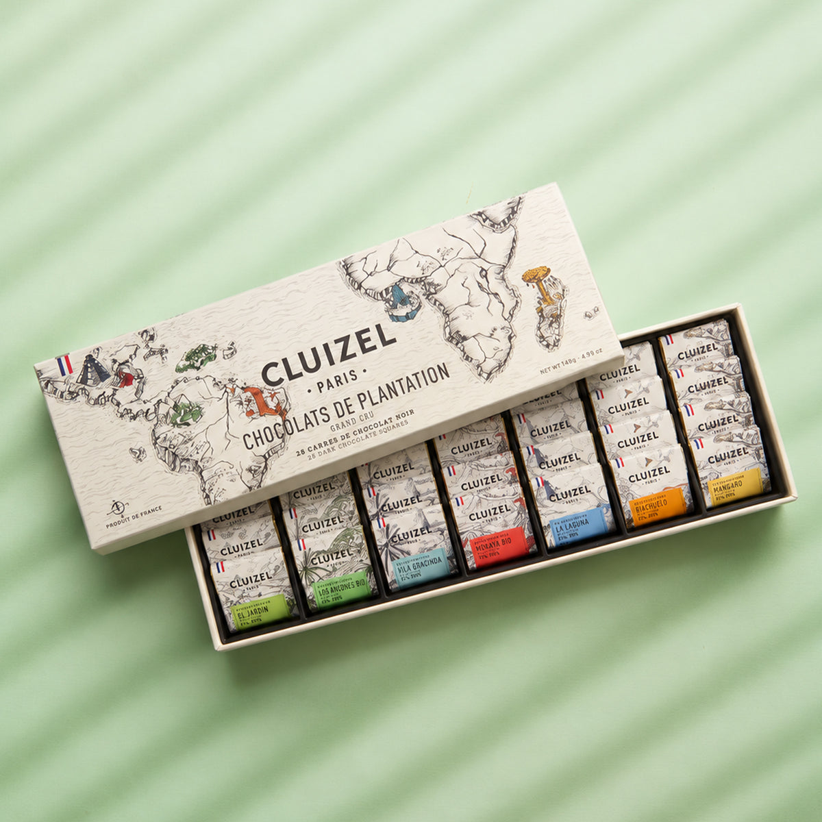Open Michel Cluizel single-estate gift box of mini chocolate bars, with an illustrated map lid, on a mint green background.