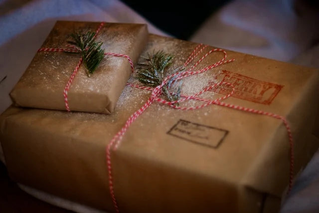 Two brown paper-wrapped gifts tied with red and white twine, each adorned with a small pine sprig.