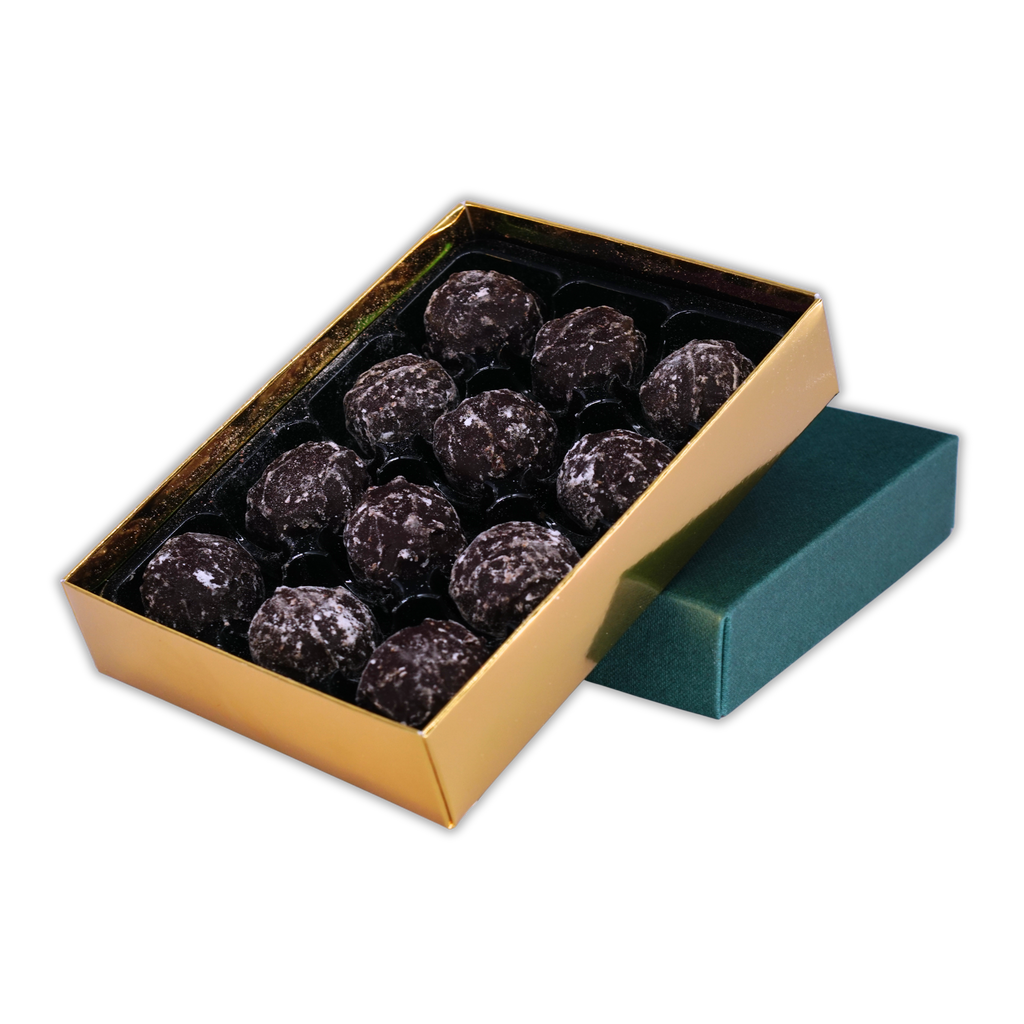 Twelve NearyNogs dark chocolate truffles arranged in an open gold box beside a green lid on a black background.