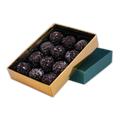 Twelve NearyNogs dark chocolate truffles arranged in an open gold box beside a green lid on a black background.