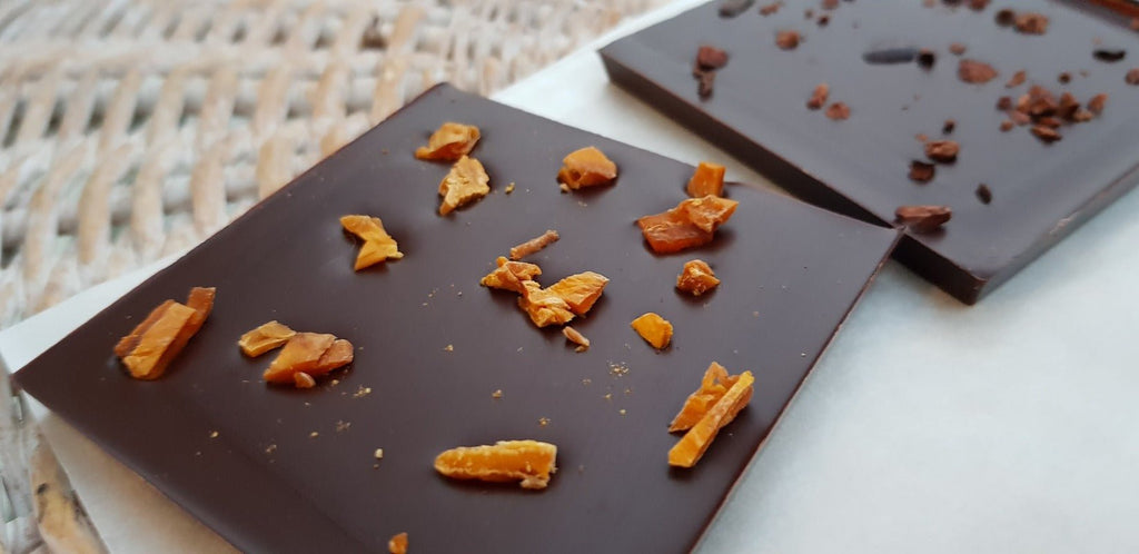 Dark chocolate bar topped with pieces of dried mango on a white surface next to a woven basket