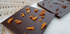 Dark chocolate bar topped with pieces of dried mango on a white surface next to a woven basket
