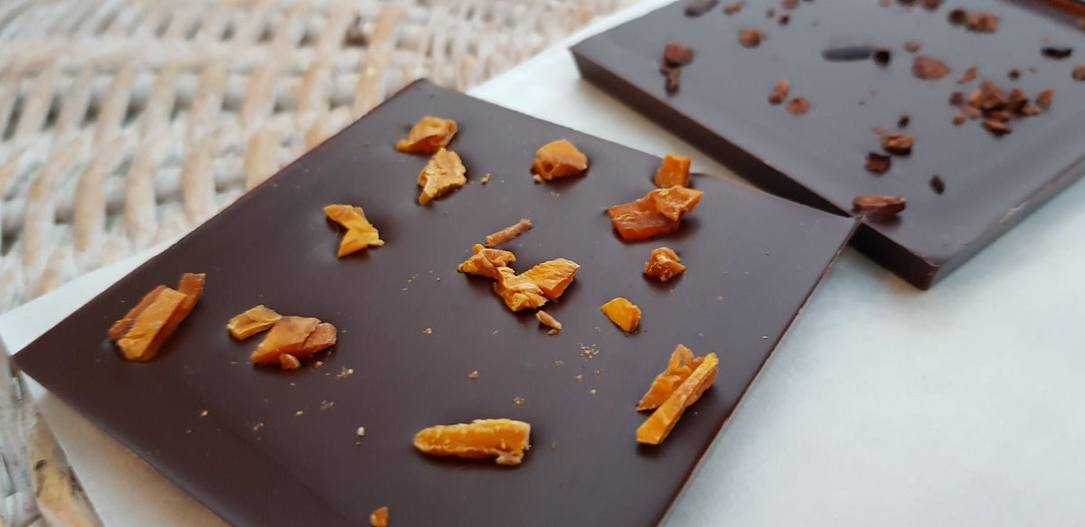 Dark chocolate bar topped with pieces of dried mango on a white surface next to a woven basket