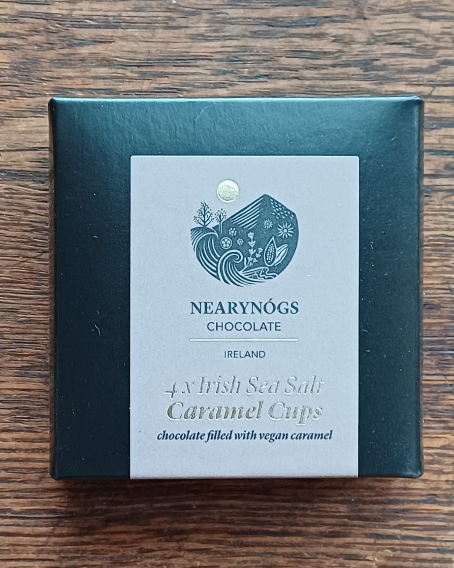 A small black box of NearyNogs Irish Sea Salt Caramel Cups resting on a textured wooden table