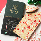 Green Moka Origins peppermint box beside white-topped bark pieces flecked with crushed candy cane.