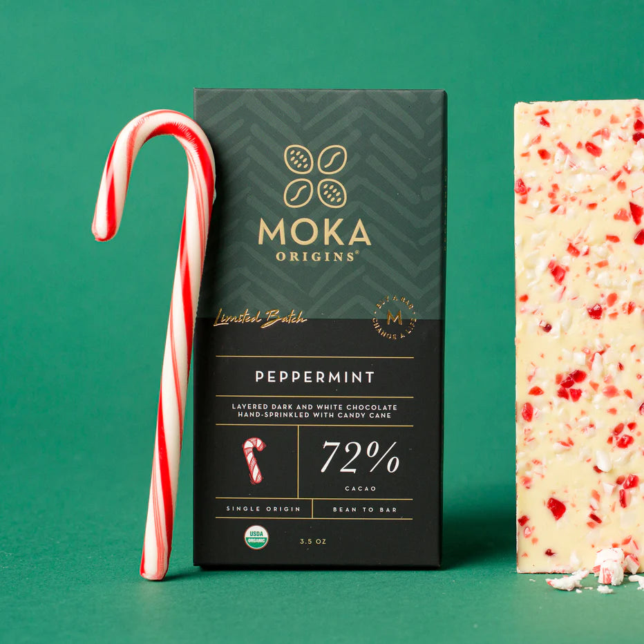 Moka Origins peppermint box against green with a candy cane and a slab of candy-cane-topped bark.