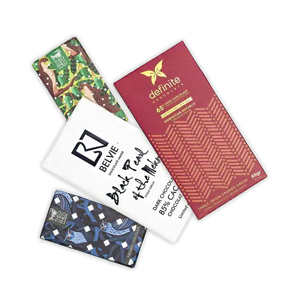 Four assorted chocolate bars with distinct packaging designs, including a green and brown illustrated wrapper, a red geometric-patterned bar from definite chocolate, a white minimalist label featuring ’black pearl of the mole’ by belvie chocolates, and a