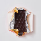 Dark chocolate bar with oval-relief pattern half unwrapped from gold and silver foil on a pale background