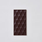 Unwrapped dark chocolate bar with rows of oval-relief circles on a light grey background