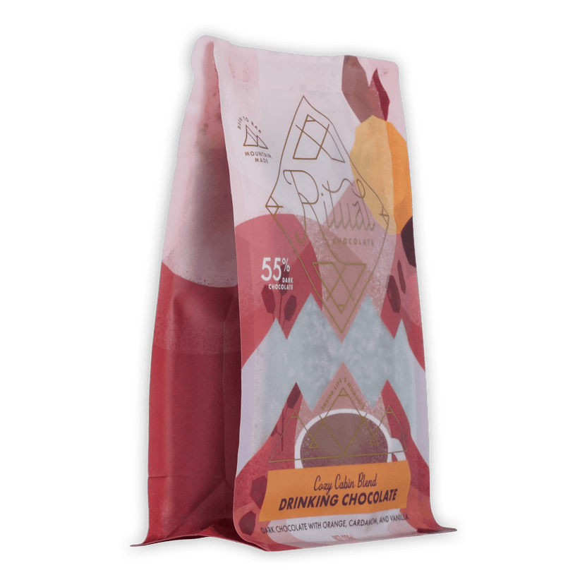 A vibrant pink and white bag of ariana’s cozy cabin blend ritual drinking chocolate 55 percent with geometric orange accents