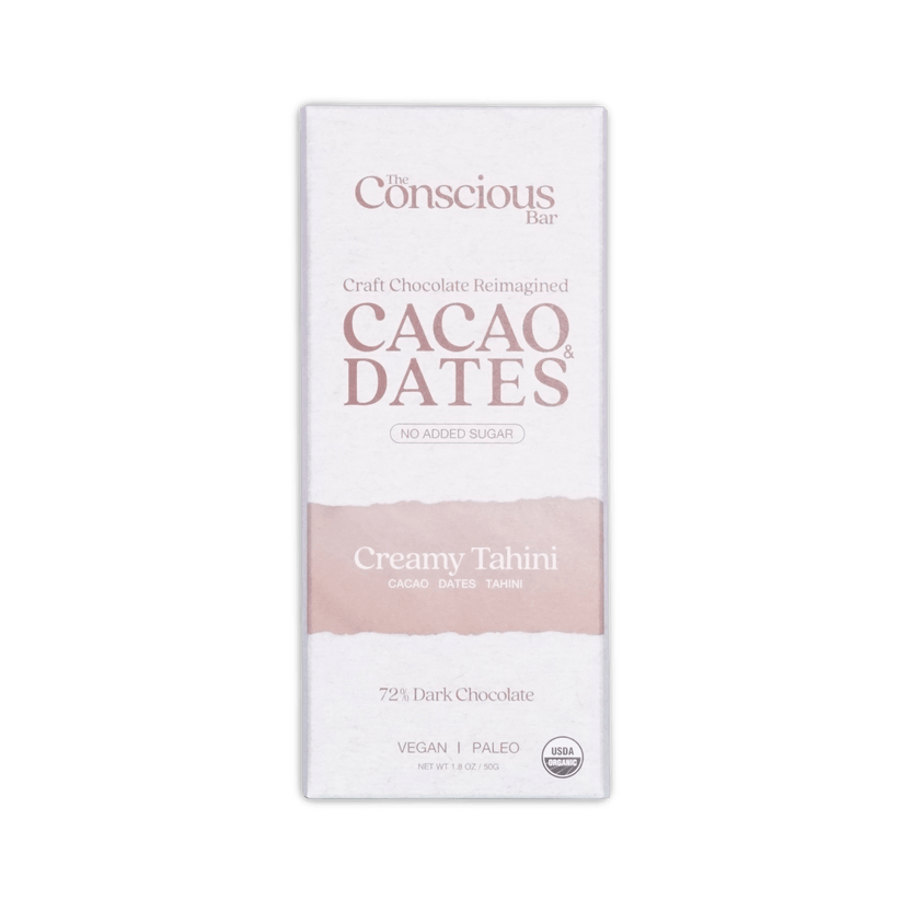 A white rectangular package of the conscious bar dark creamy tahini 72 percent cacao and dates chocolate bar with pink stripe