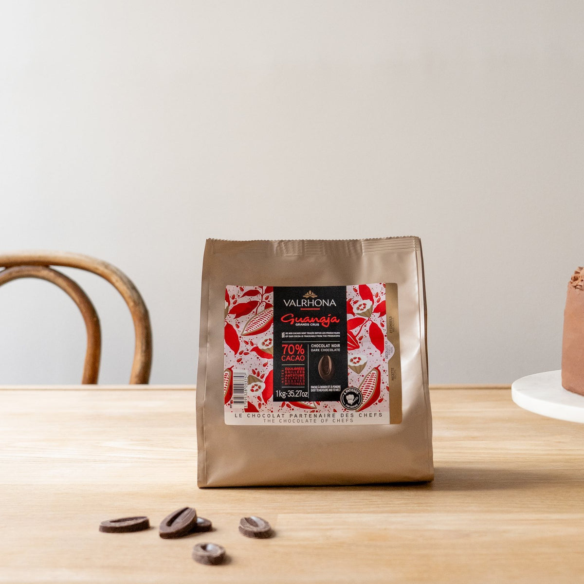 Valrhona Guanaja 70% dark chocolate feves 1kg bag beside a chocolate layer cake