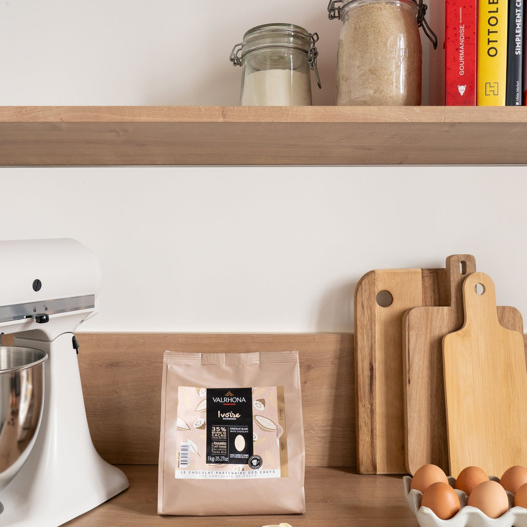 Valrhona Ivoire 35% white chocolate feves bag on a kitchen shelf with jars and cookbooks