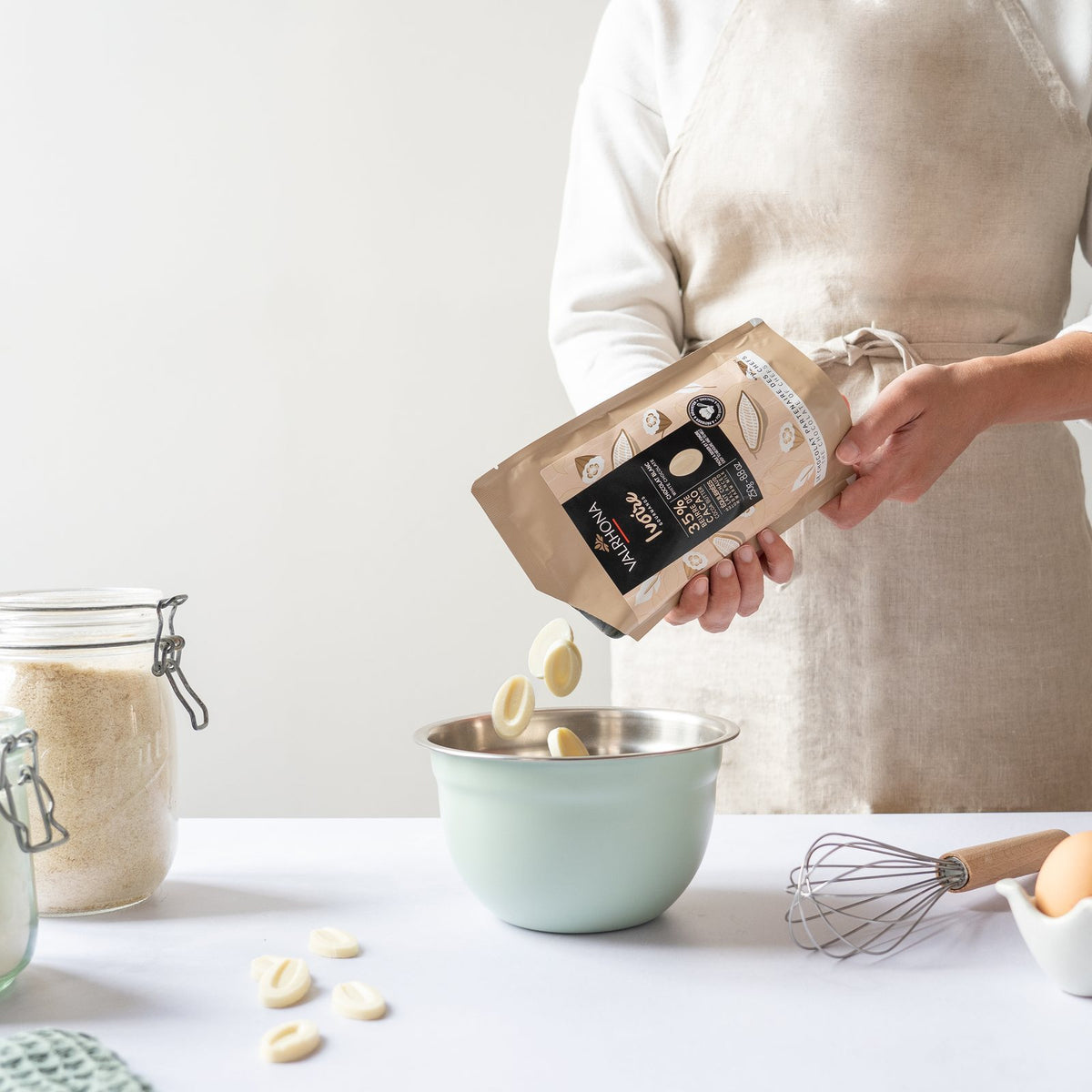 Pouring Valrhona Ivoire 35% white chocolate feves from the 250g pouch into a bowl