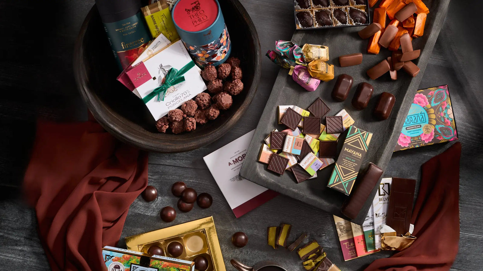A collection of assorted chocolates in colorful packaging, including a decorative tin and various bars with intricate designs.