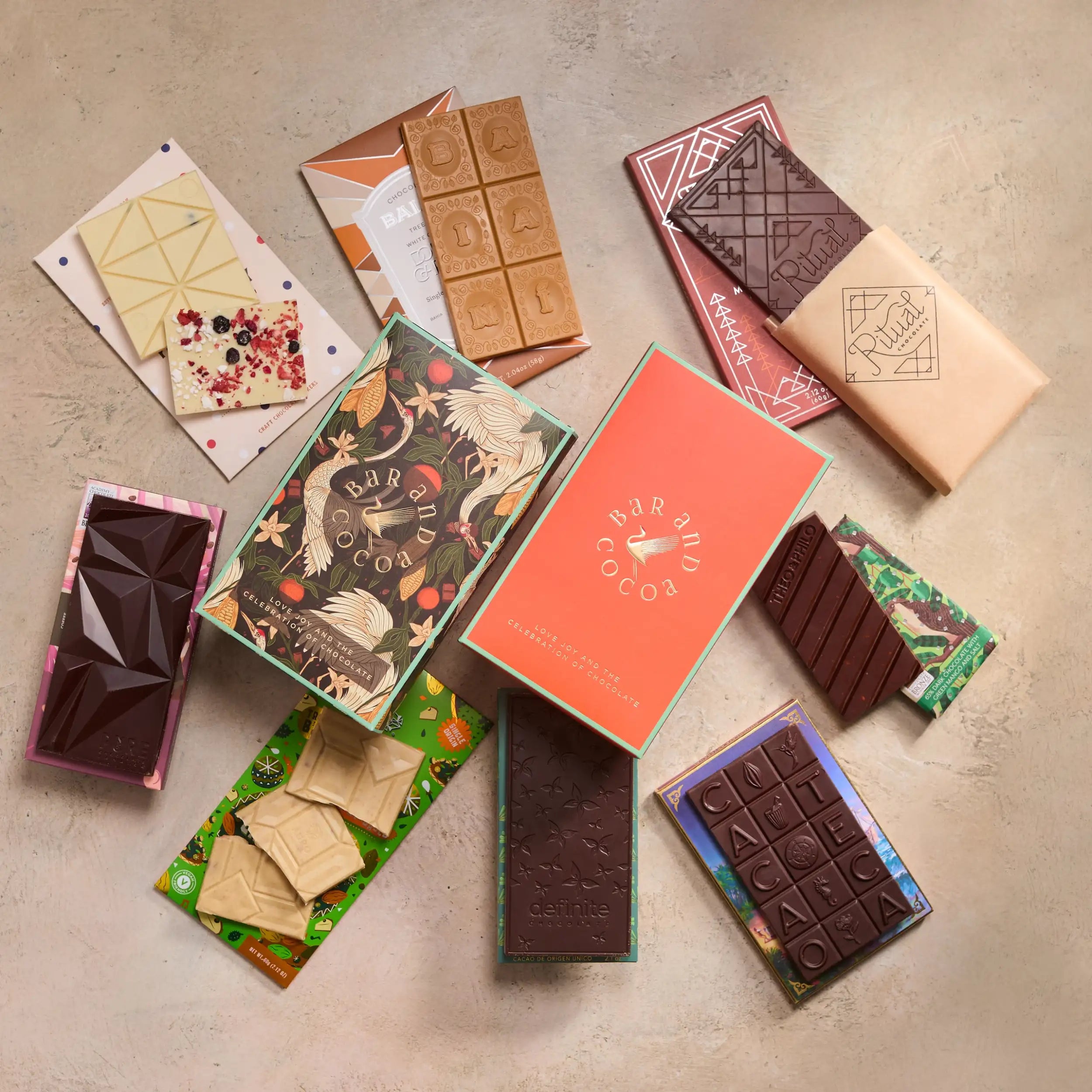 A collection of assorted chocolate bars from bar and cocoa, featuring various designs including geometric patterns, floral motifs, and colorful packaging in shades like orange, green, pink, and beige.