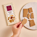 Hand holding broken Domori White Chocolate w/ Caramel & Pecans bar with packaging